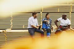 Blue-collor workers during lunch break. Laughing. Female Asian, male African-American and male Caucasian. Checkered shirt and white T-shirt. Primary color white. Secondary color yellow.