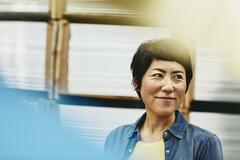 Female Asian worker in logistics environment. Blue-collar. Smiling. Primary color blue. Secondary color white/cream.