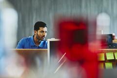 Man in polo shirt, looking at his desktop. India. Primary color: red.