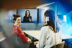 Two business women and a man in an office having a Hangout. Primary color: blue.