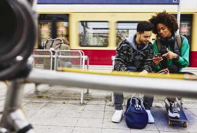Man and woman looking at phone while sitting on a bench on a train platform.