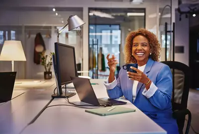 Female with blue blazer sitting behind computer at a desk, smiling to a person