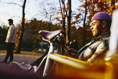 Man sitting on a bench with his bike next to him, looking at his phone.