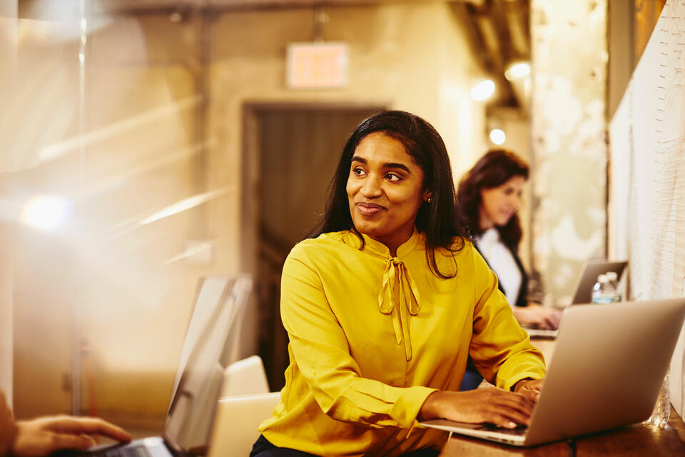 A woman working on a computer in a yellow sweater